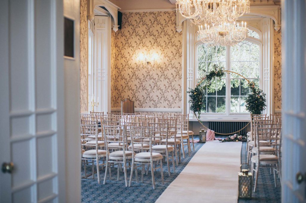 The Cardeston Suite (a grand hall) is set with limewash chiavari chairs and an ivory aisle carpet ready for an indoor wedding ceremony.