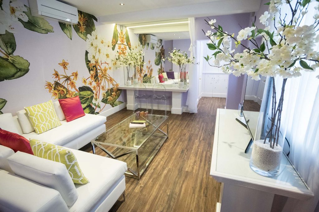 The Orchard Suite Lounge from afar; the white leather sofa with bright cushion and a hair and make up station can be seen