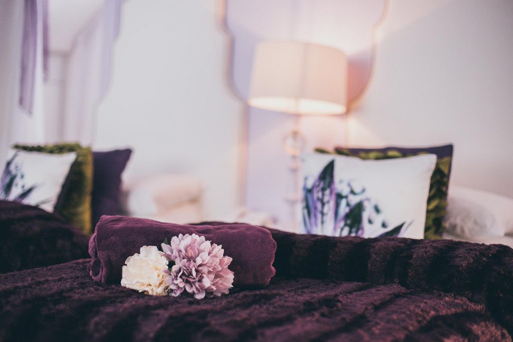 A close up of the Orchard Suite twin bedroom with luxe violet throws and floral cushions
