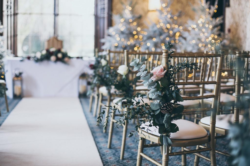 The ceremony room at Rowton Castle is set up for a ceremony with gold chairs and an ivory carpet. The end of aisle chairs are dressed with winter foliage