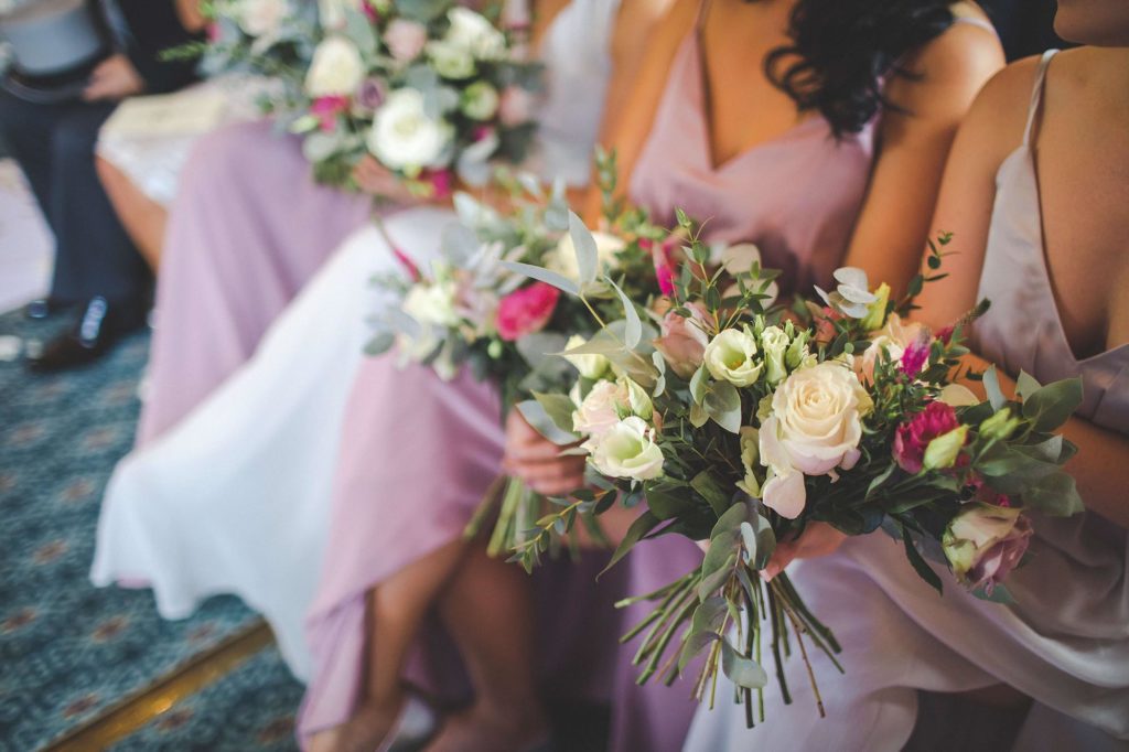 The bridesmaids are photographed up close wearing pink silk dresses and holding bouquets full of summer flowers