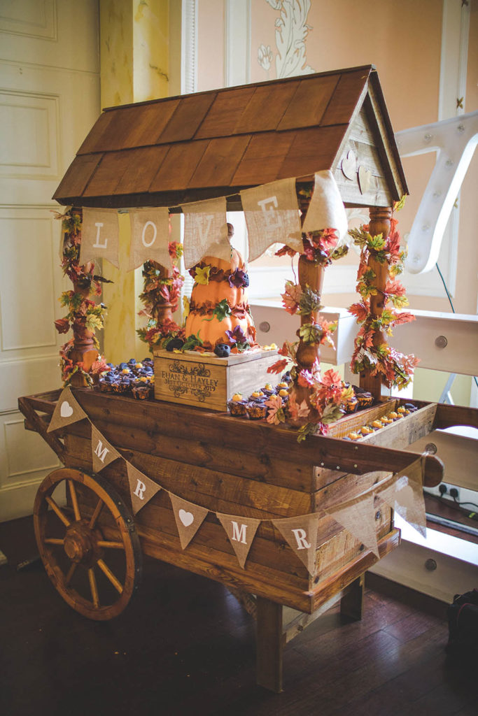 Rustic touches were chosen for this autumn wedding. A wooden cart is photographed with a three tiered pumkin wedding cake on top