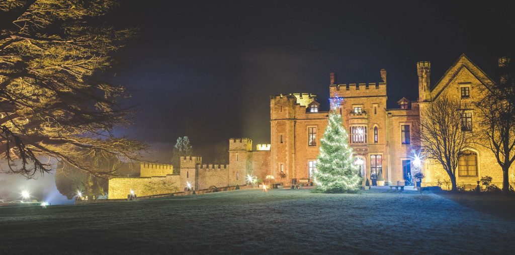 Rowton Castle captured at night, there is frost on the ground. The Christmas tree at the front of the castle sparkles with fairy lights