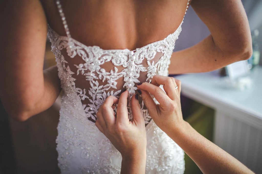 The buttons of an intricate lace wedding dress are done up