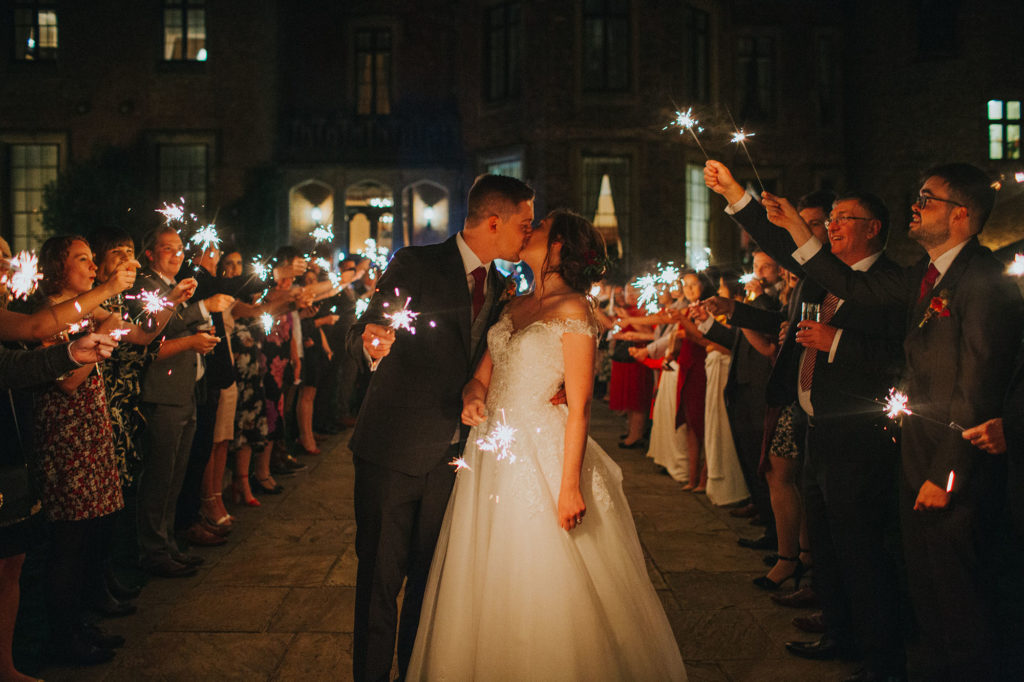 Bride and groom kiss whilst guests line up with sparklers around them