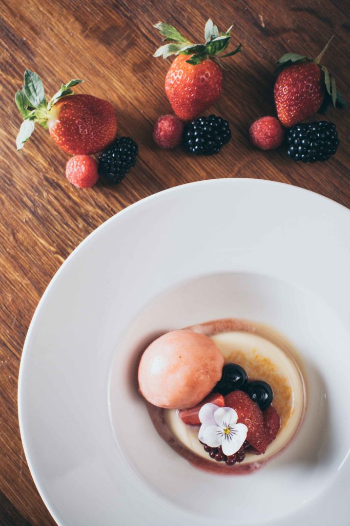 Orange panna cotta with fruit sorbet is plated with summer berries