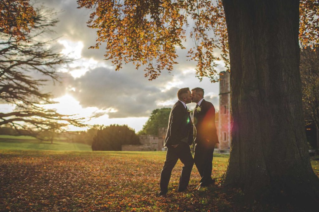 Groom's Christian and Tom are photographed kissing in front of the castle on an Autumn's day