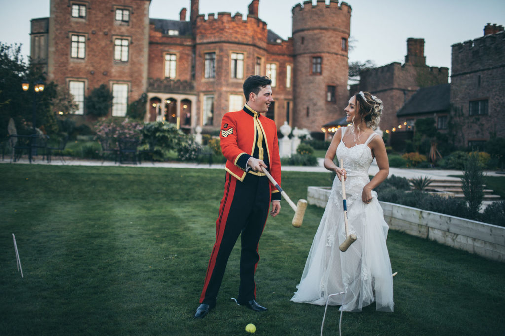 The bride and groom play croquet in the castle gardens, the castle acts as a beautiful backdrop