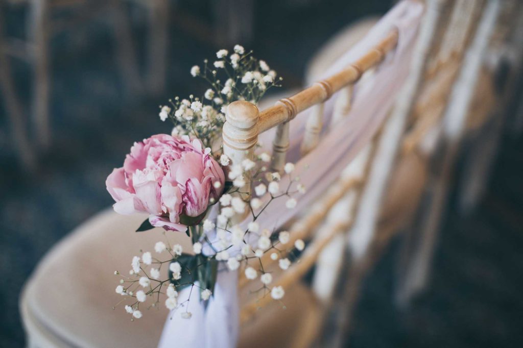 Summer peonies and gypsophila dress the chairs in this indoor ceremony set up