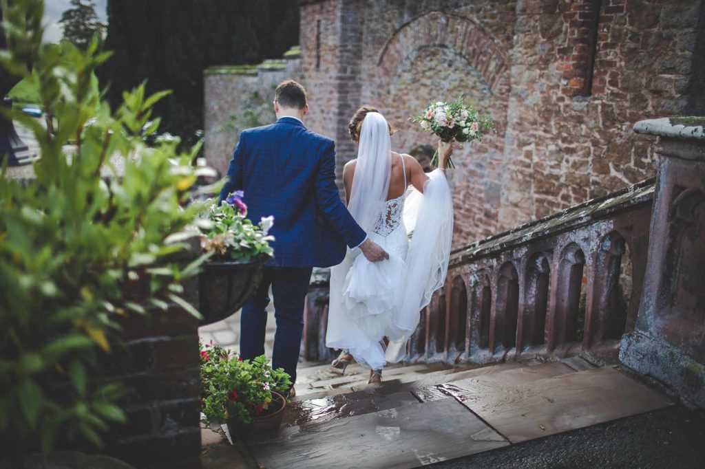 The Bride and Groom (Gemma & James) are photographed from behind whilst walking down the castle's front steps. James holds Gemma's dress