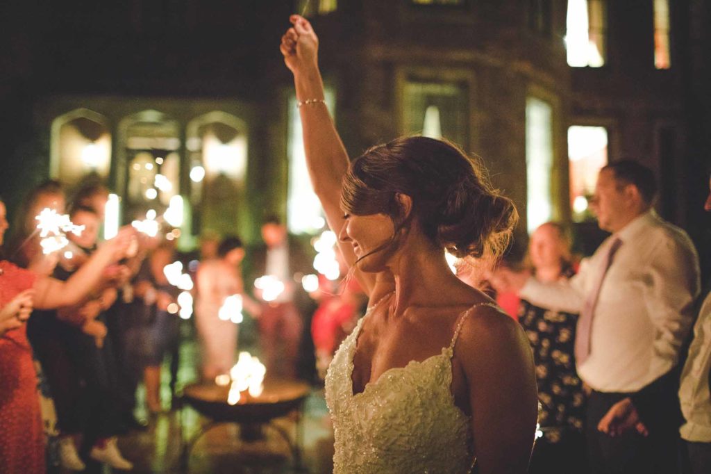 Bride Gemma dances in the gardens of Rowton Castle. She is front of the fire pit and guests around her enjoy sparklers
