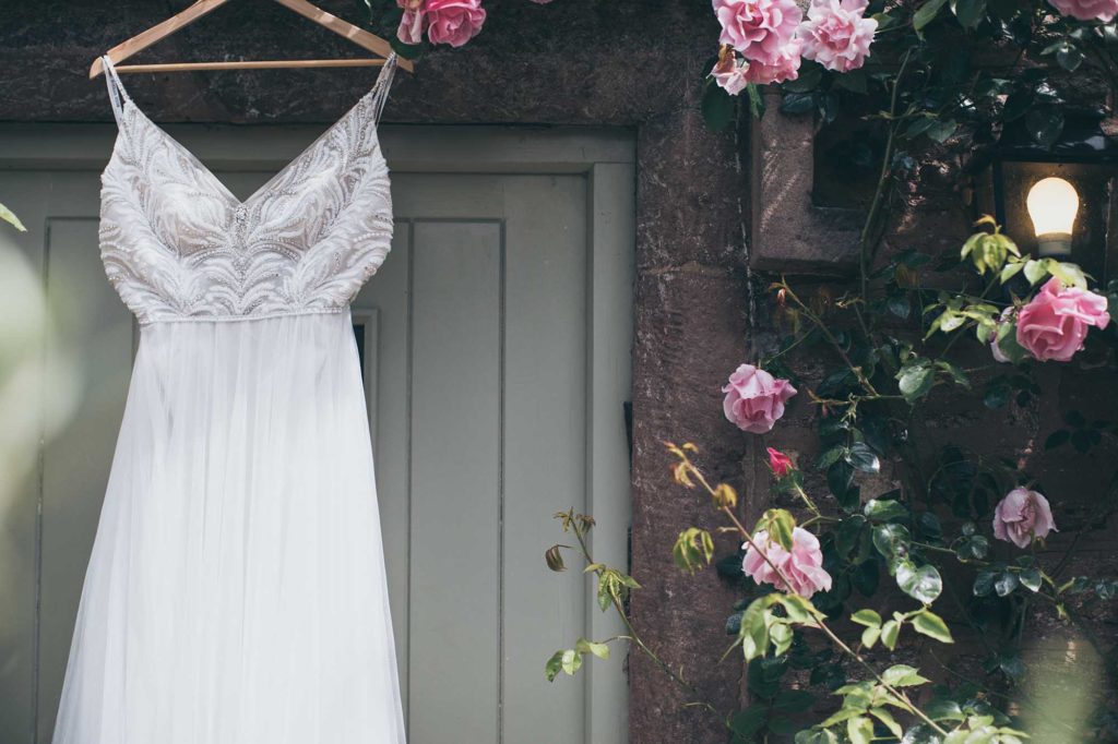 A brides dress has been hung at the door of the orchard suite, fluffy pink climbing roses frame the picture