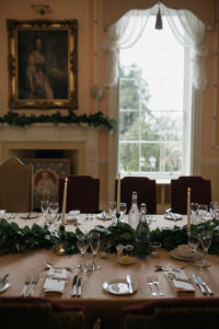 The Cardeston Room is photographed set for an intimate wedding. Plush velvet red chairs, white linen candles and green foliage all feature