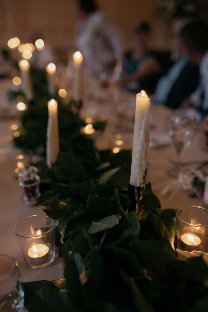 Close up of the intimate wedding breakfast table, Pillar candlesticks, tea lights and green foliage are laid out in the centre