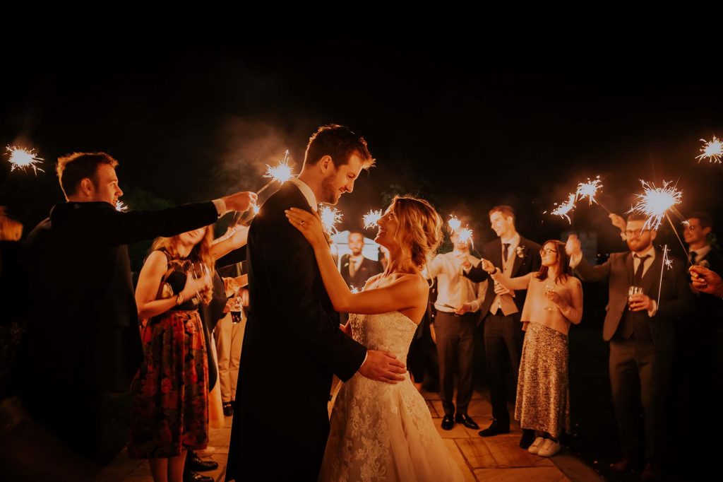 The Bride and Groom embrace whilst guests enjoy sparklers around them