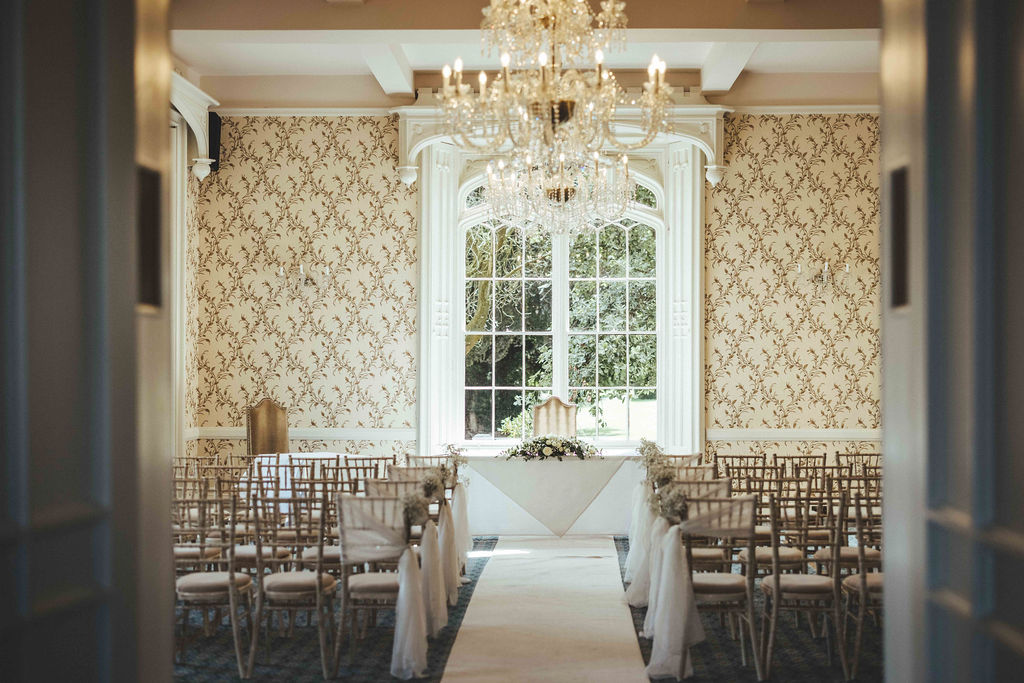 The Cardeston Suite is elegantly dressed with ivory carpet and limewash chiavari chairs for an indoor wedding. Sunlight floods the room through the large windows
