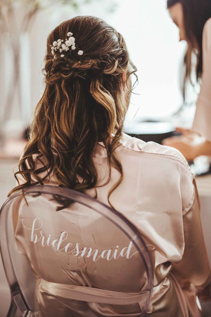 A bridesmaid in a pink silk dressing gown has her curly hair pinned ready for the wedding ceremony