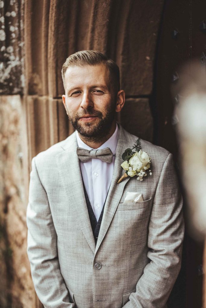 Groom Dan is photographed in his beige linen suit in front of the old walls of the castle