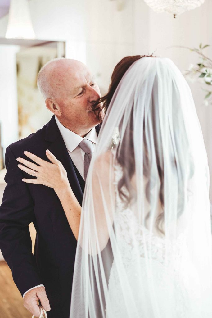The father of the bride kisses his daughter of the cheek ahead of her wedding ceremony
