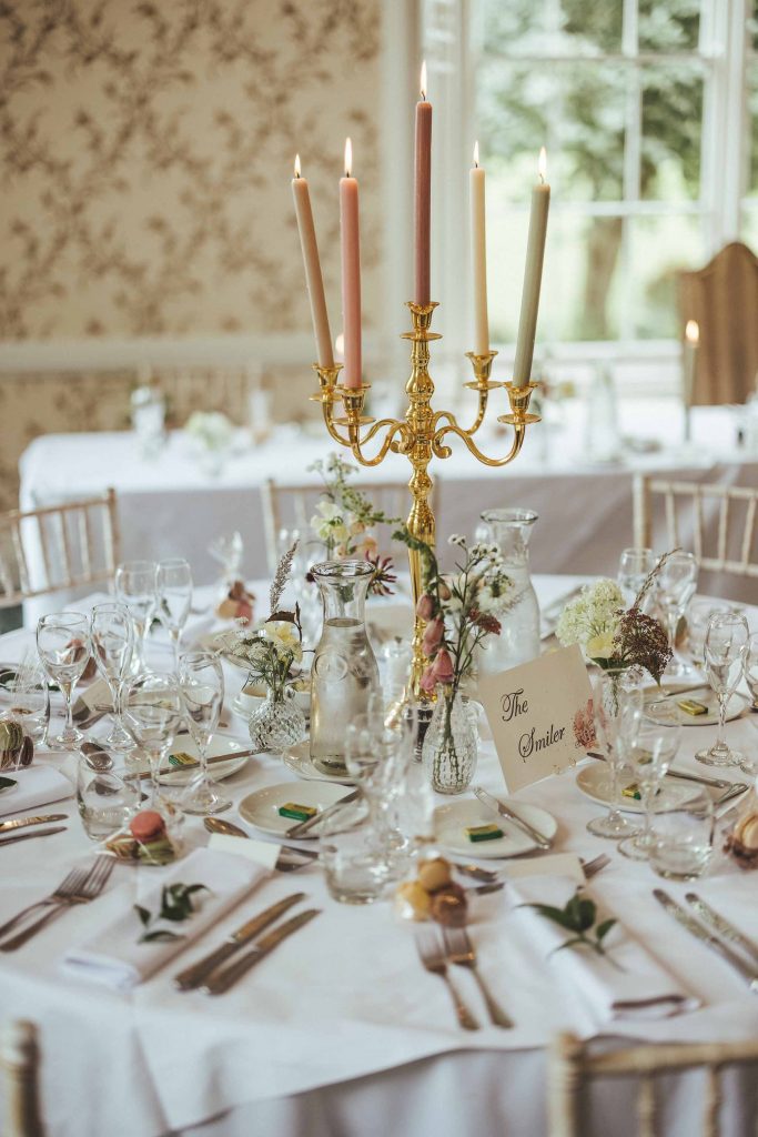 A close of the Wedding Breakfast table with white linens, silver cutlery and elegant glassware. A gold candelabra with pastel candles completes the table