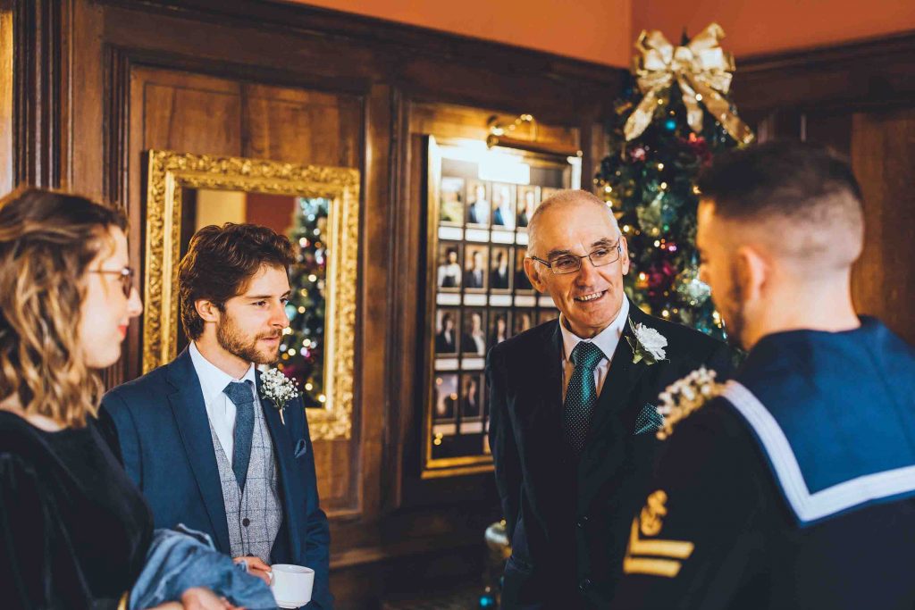 The groom (dressed in his navy uniform) chats to guests in front of the christmas tree in the castle reception prior to the wedding ceremony