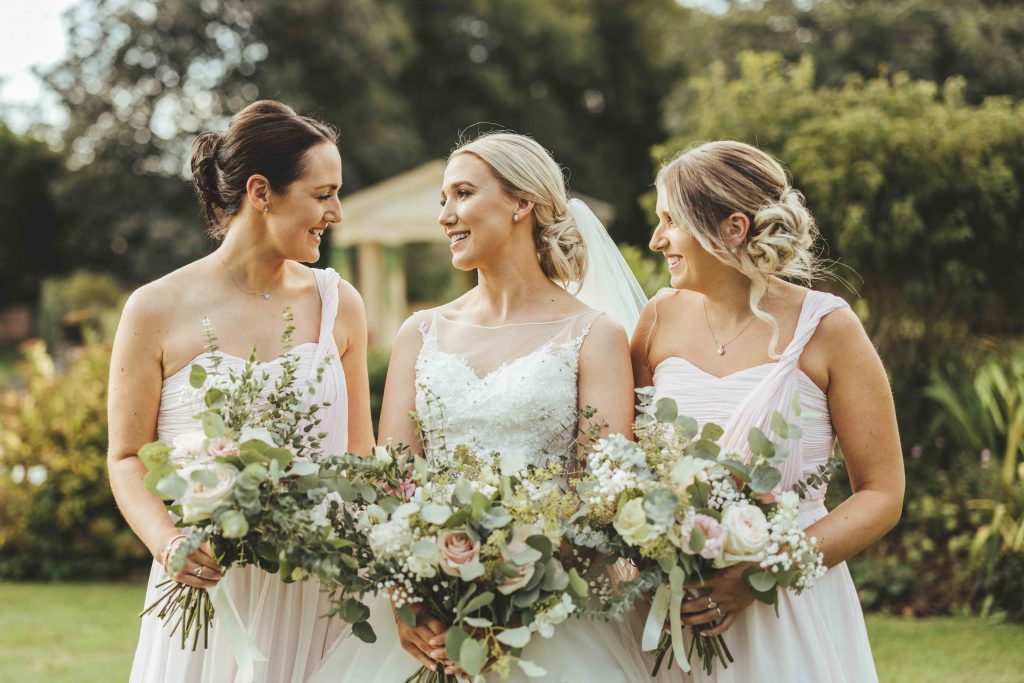 Bride and her bridesmaids pose in front of the linden belvedere on this summers wedding day. The dresses are light pink and the bouquets filled with summer blooms