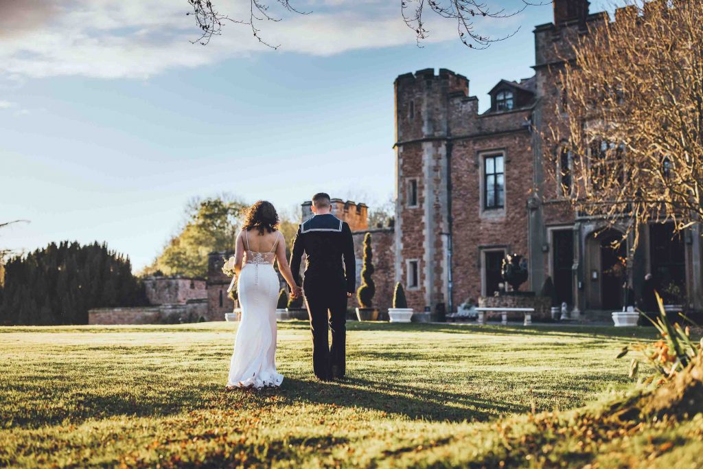 Holly and George walk in the castle grounds on their winters wedding day. The front of the castle can bee seen