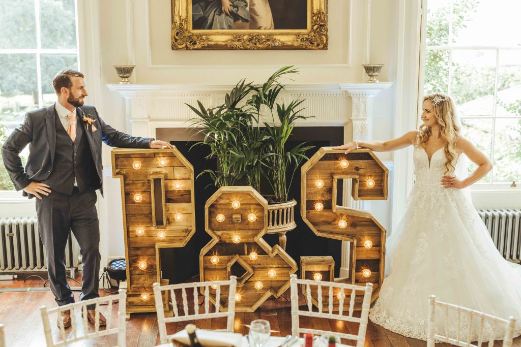 Groom Paul and Bride Sophie pose in front of rustic P & S love letters on their wedding day