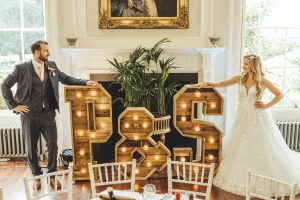 Groom Paul and Bride Sophie pose in front of rustic P &amp; S love letters on their wedding day