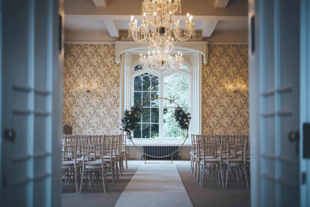 Rowton Castle's indoor ceremony space; dressed simply with limewash chiavari chairs, and ivory aisle carpet and floral adorned gold moongate