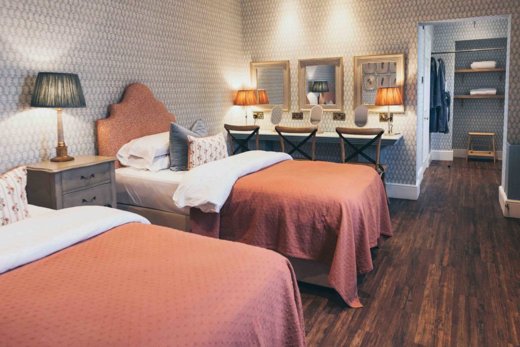 The Orchard Suite Twin Beds are Dressed with Coral Throws, Cushions and have Intricate Coral Headboards; a Salon beyond this has Three Mirrors and Cross Back Chairs