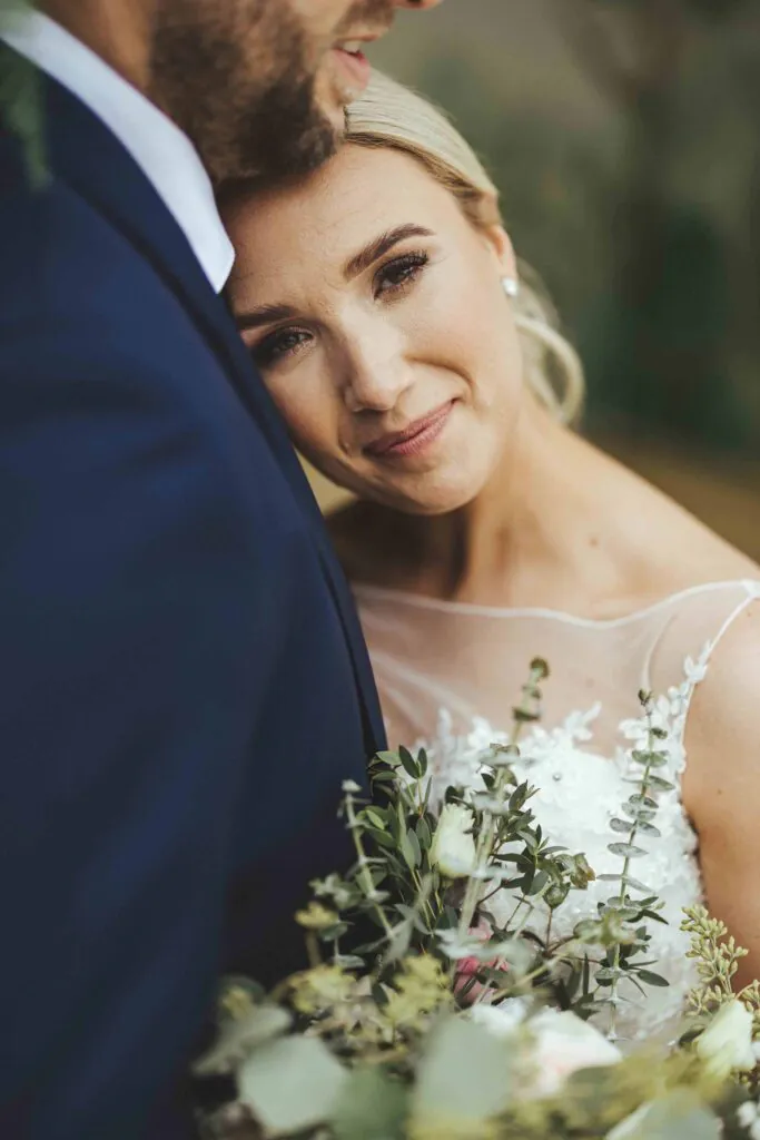 Bride holding a bouquet and resting her head against the groom during an intimate wedding portrait at Rowton Castle.