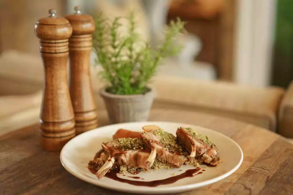 Three lamb chops arranged on a white plate with couscous, vegetables, and a dark jus.