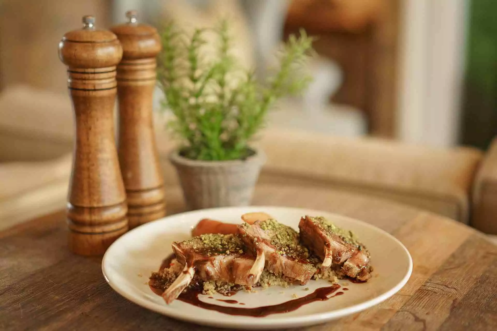 Three lamb chops arranged on a white plate with couscous, vegetables, and a dark jus.