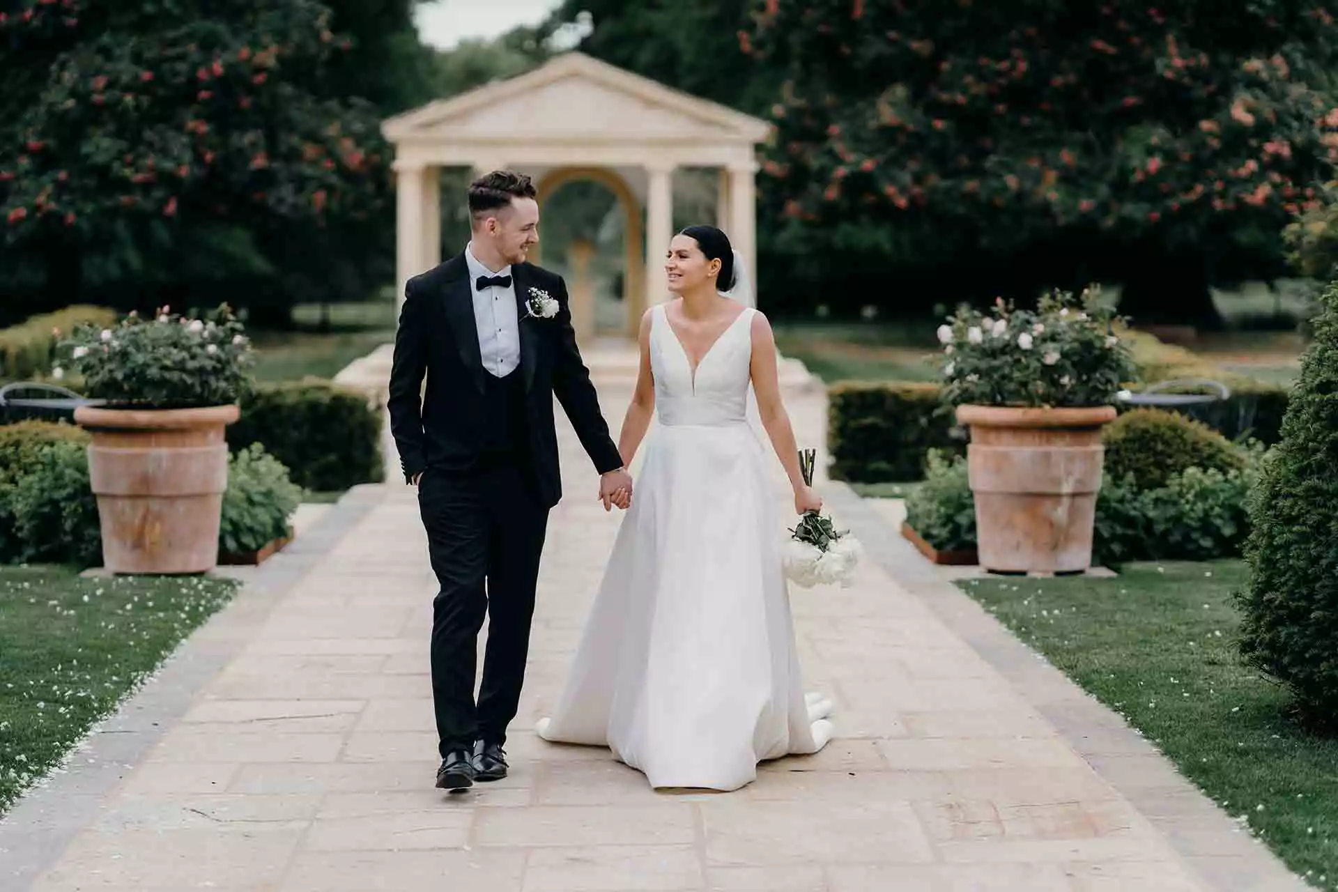 Bride and groom walking together along a stone pathway in the formal gardens at Rowton Castle.