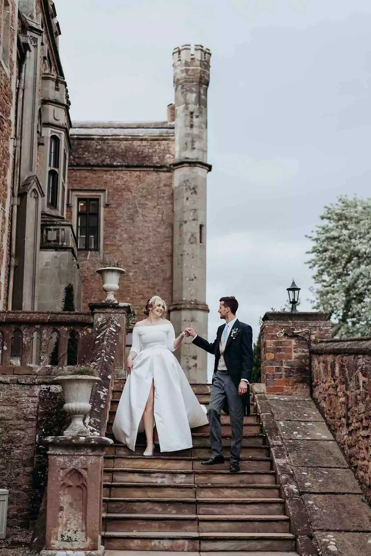 Bride and groom holding hands as they walk down the historic stone steps outside Rowton Castle.