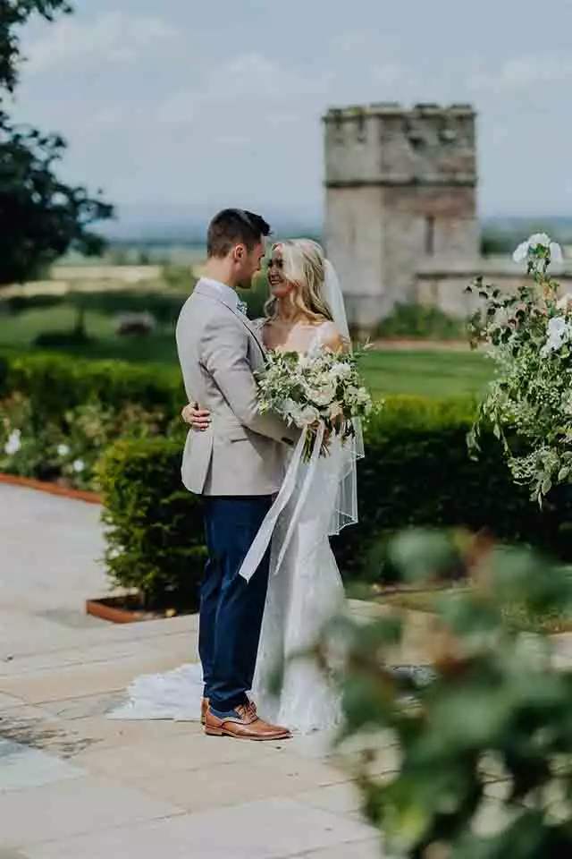 A bride and groom embracing in the landscaped gardens of Rowton Castle, a luxury Shropshire wedding venue.