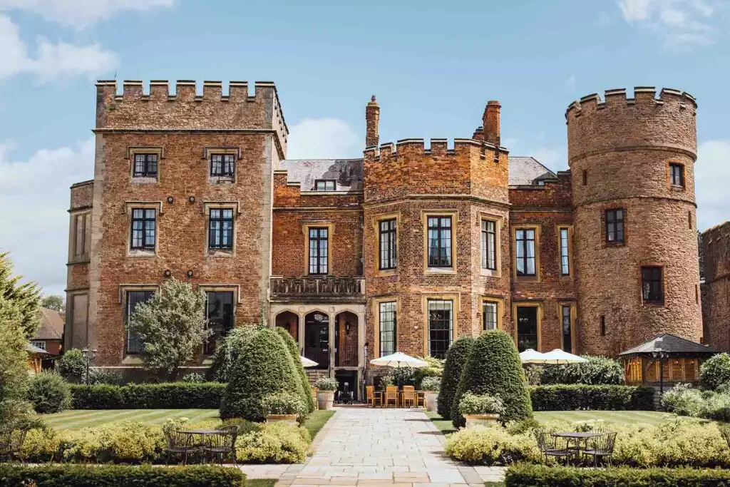 Front view of Rowton Castle in Shropshire with manicured gardens, historic brick façade and castle turrets on a sunny day.