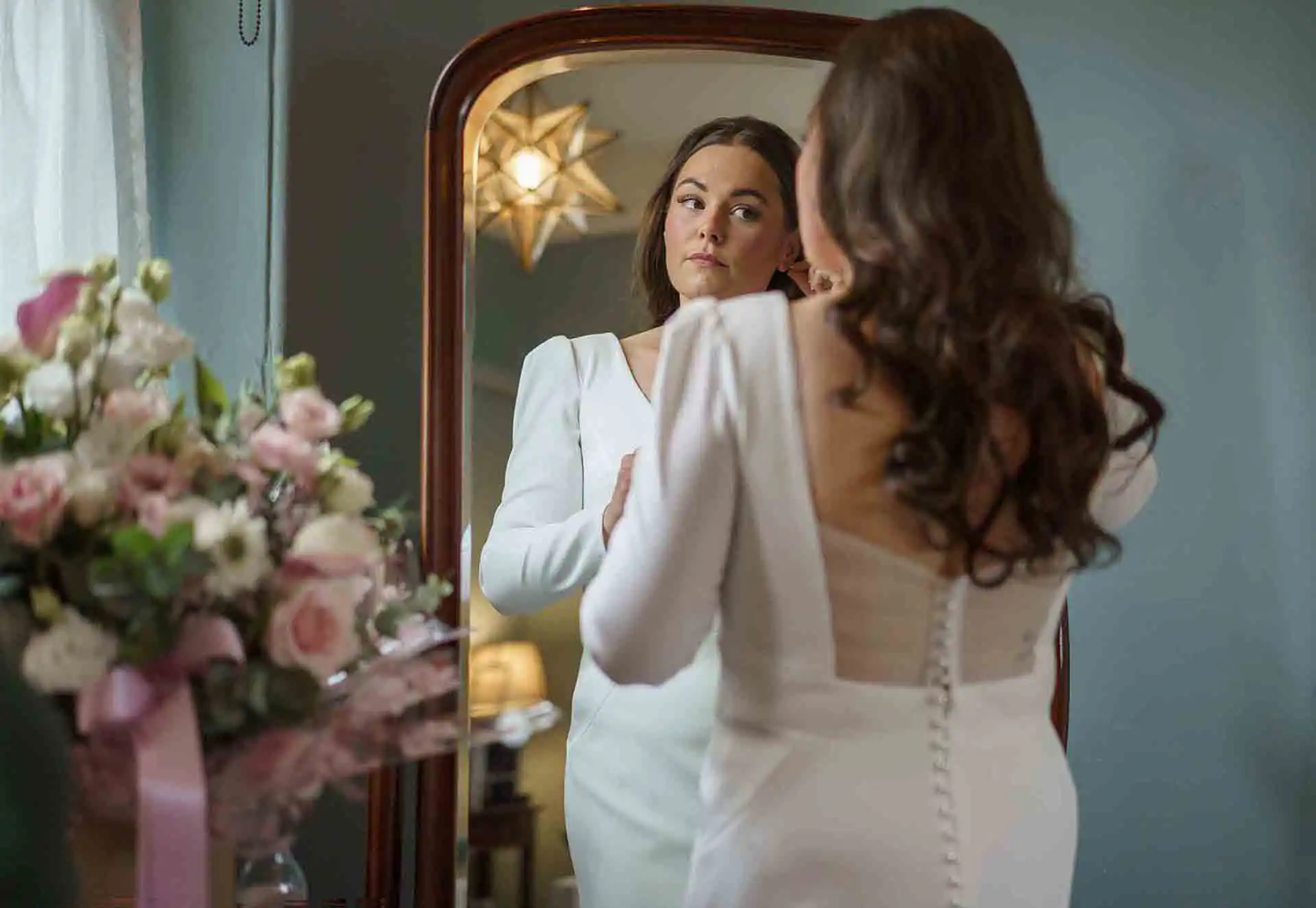 Bride adjusting her earrings while looking in the mirror