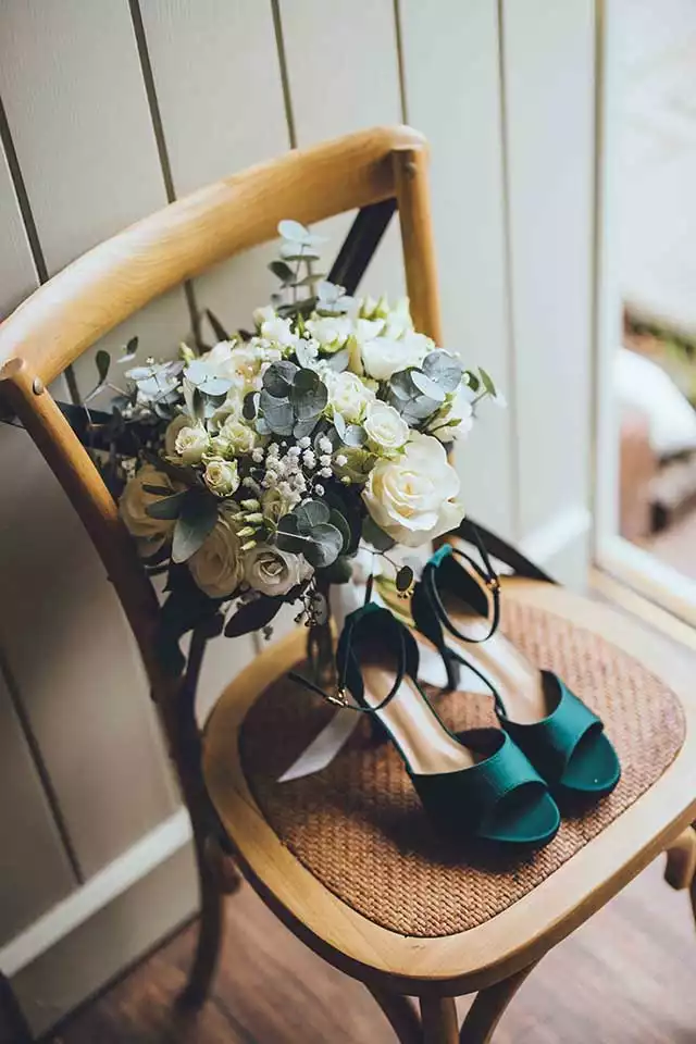 Wedding shoes and bouquet arranged on a wooden chair