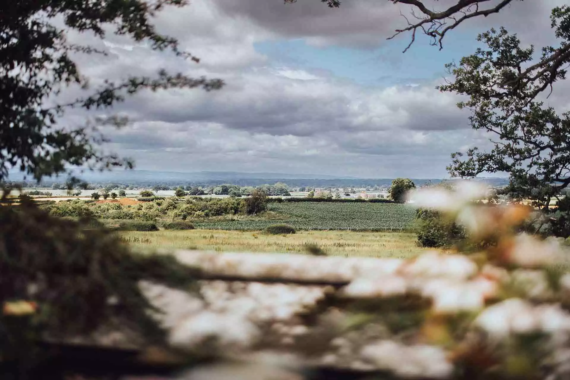 Panoramic countryside view across rolling fields and farmland surrounding Rowton Castle in Shropshire under a dramatic cloudy sky.