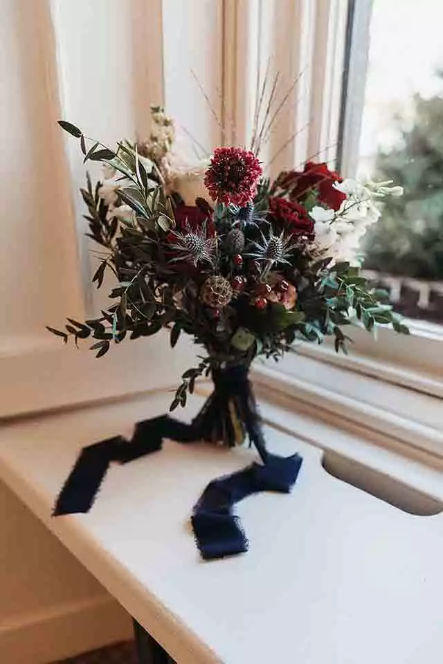 Close-up of a winter bridal bouquet featuring deep red flowers, thistles, and seasonal greenery at Rowton Castle.