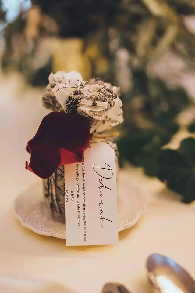 Close-up of a personalised winter wedding favour wrapped in decorative paper with a name tag, styled on a candlelit reception table at Rowton Castle.