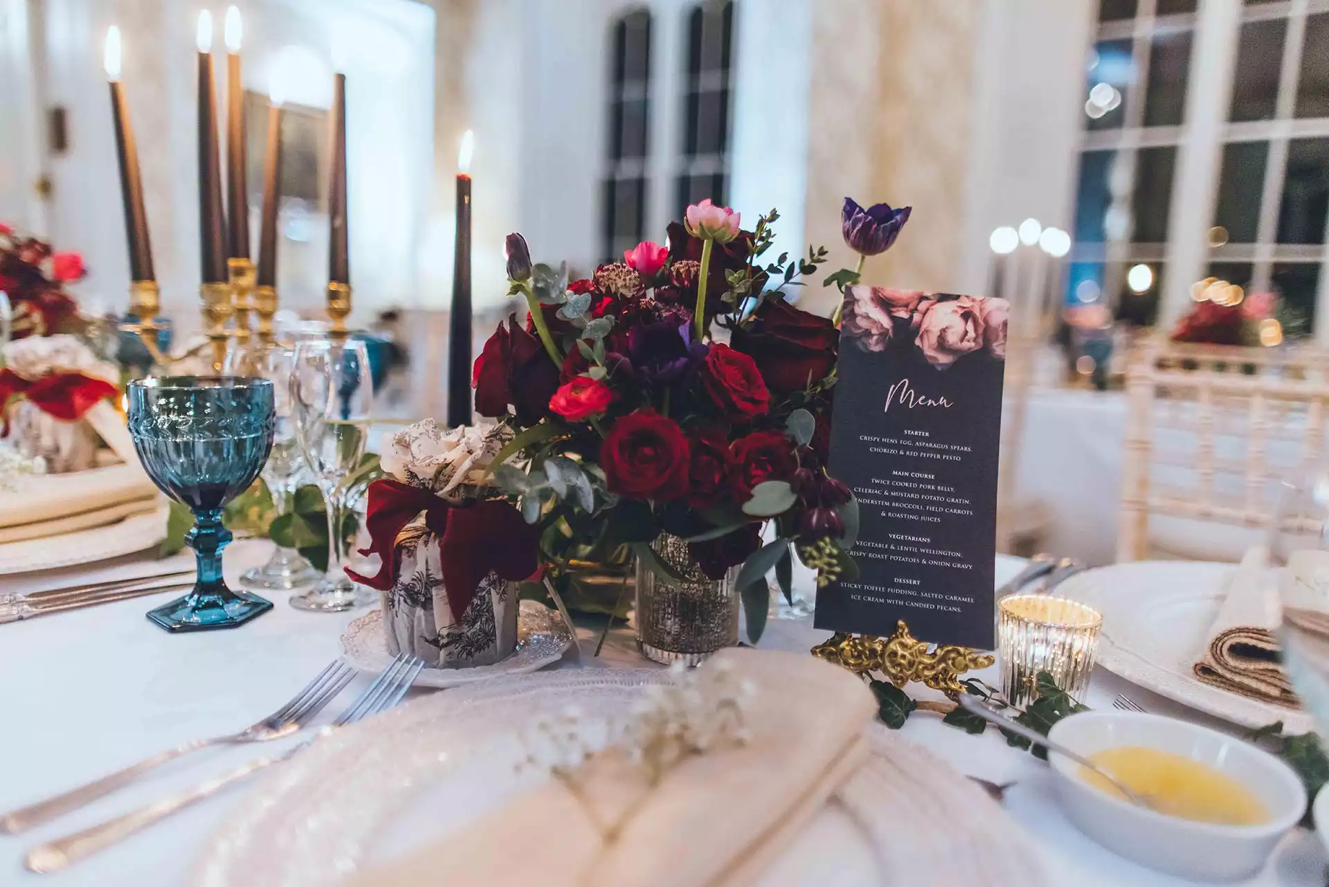 Winter wedding reception table at Rowton Castle featuring burgundy floral centrepieces, black taper candles, gold accents and printed menus.