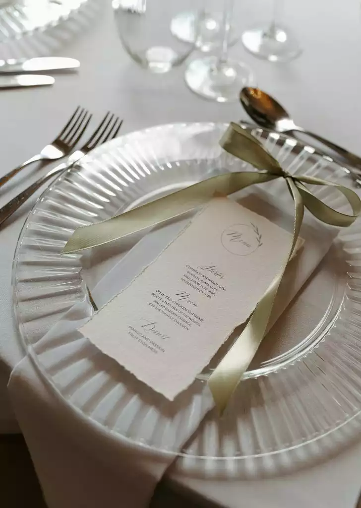 Wedding breakfast menu placed on a glass charger plate with ribbon at Rowton Castle