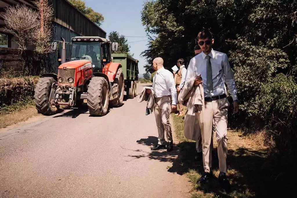 Groomsmen walking along a quiet country lane near Rowton Castle, with a red tractor parked beside farm buildings in the rural Shropshire countryside.