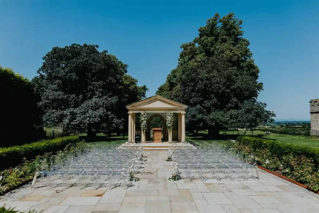Outdoor wedding ceremony setup at the Rowton Castle temple with clear guest chairs