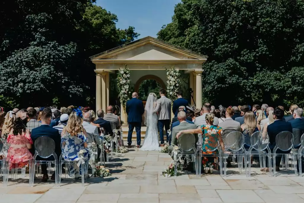 Outdoor wedding ceremony taking place at the Rowton Castle temple with guests seated on clear chairs