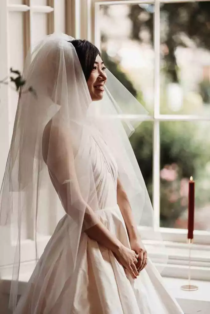 Bride in wedding dress standing beside the ceremony room window at Rowton Castle